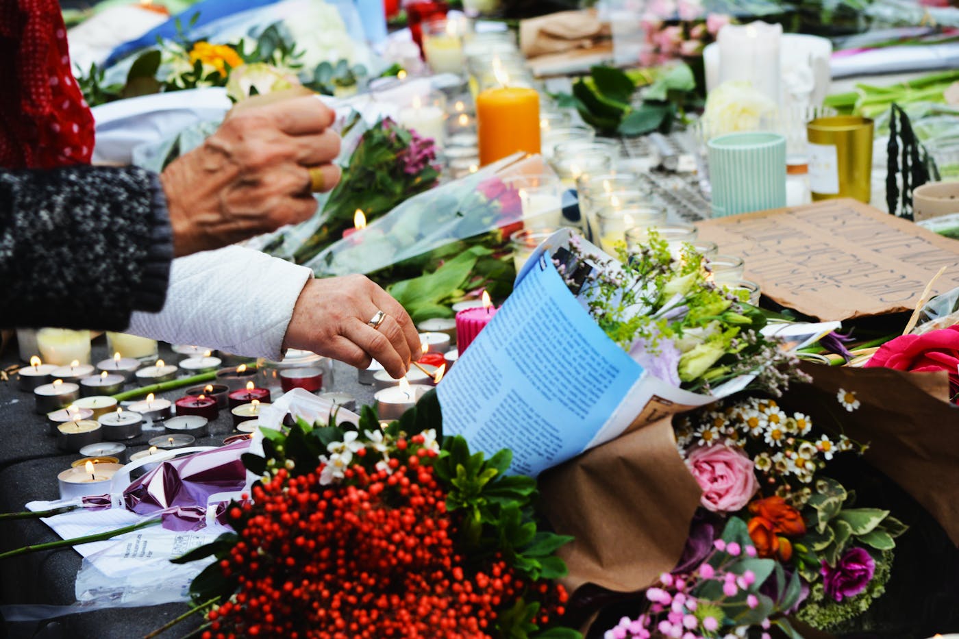 Hands lighting candles beside flowers during a memorial moment